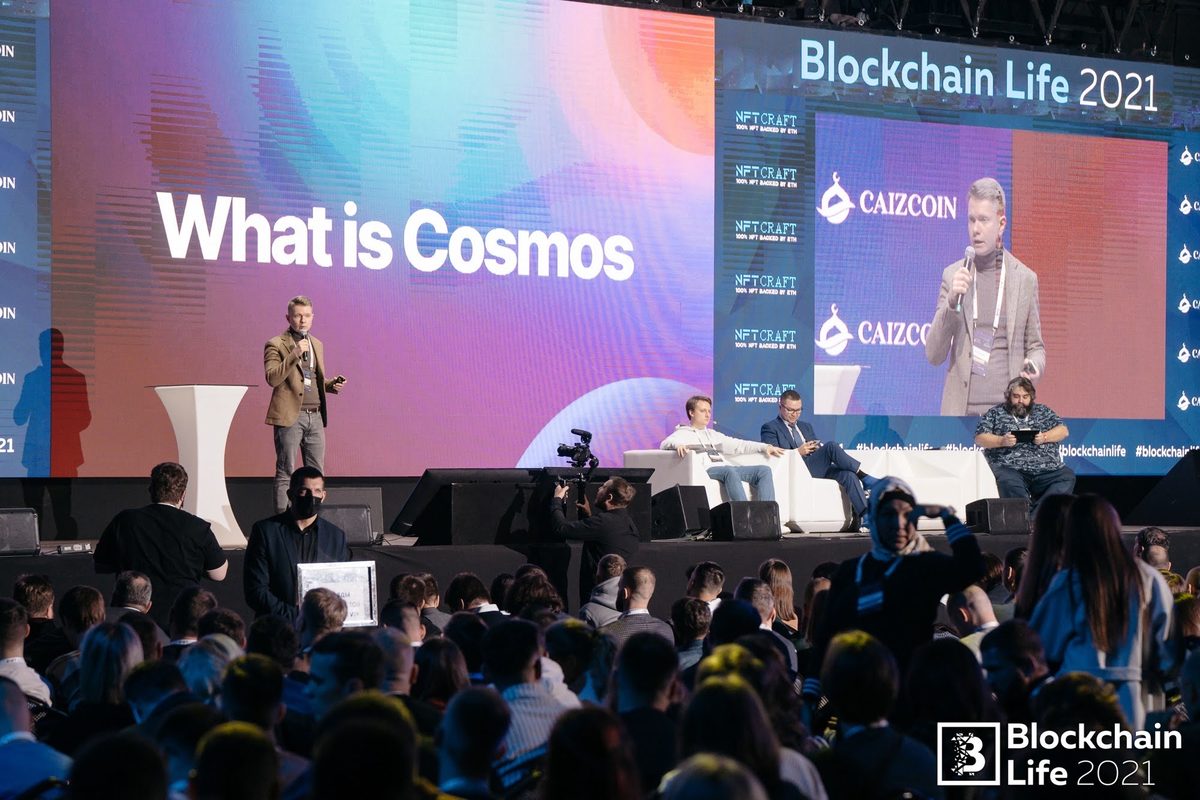 Denis on the Blockchain Life 2021 stage beside a large screen reading “What is Cosmos”