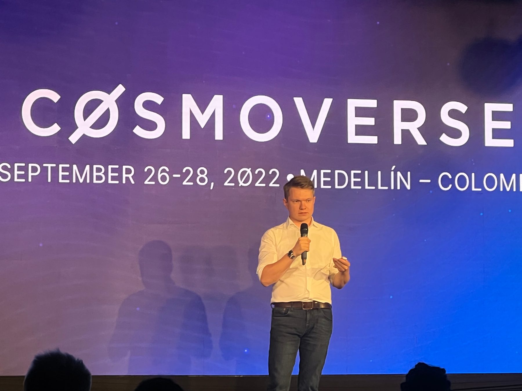 Denis speaking with a microphone in front of the Cosmoverse 2022 backdrop