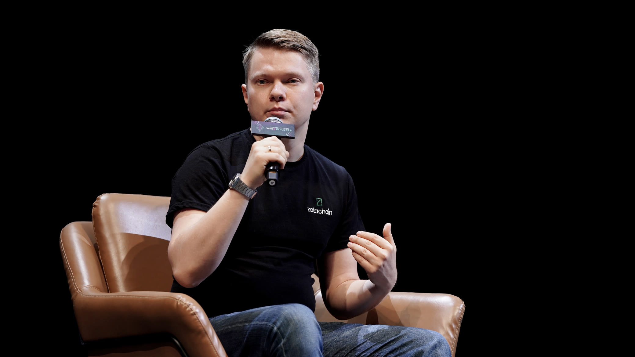 Denis on stage at ETH Hong Kong, answering into a microphone from an armchair