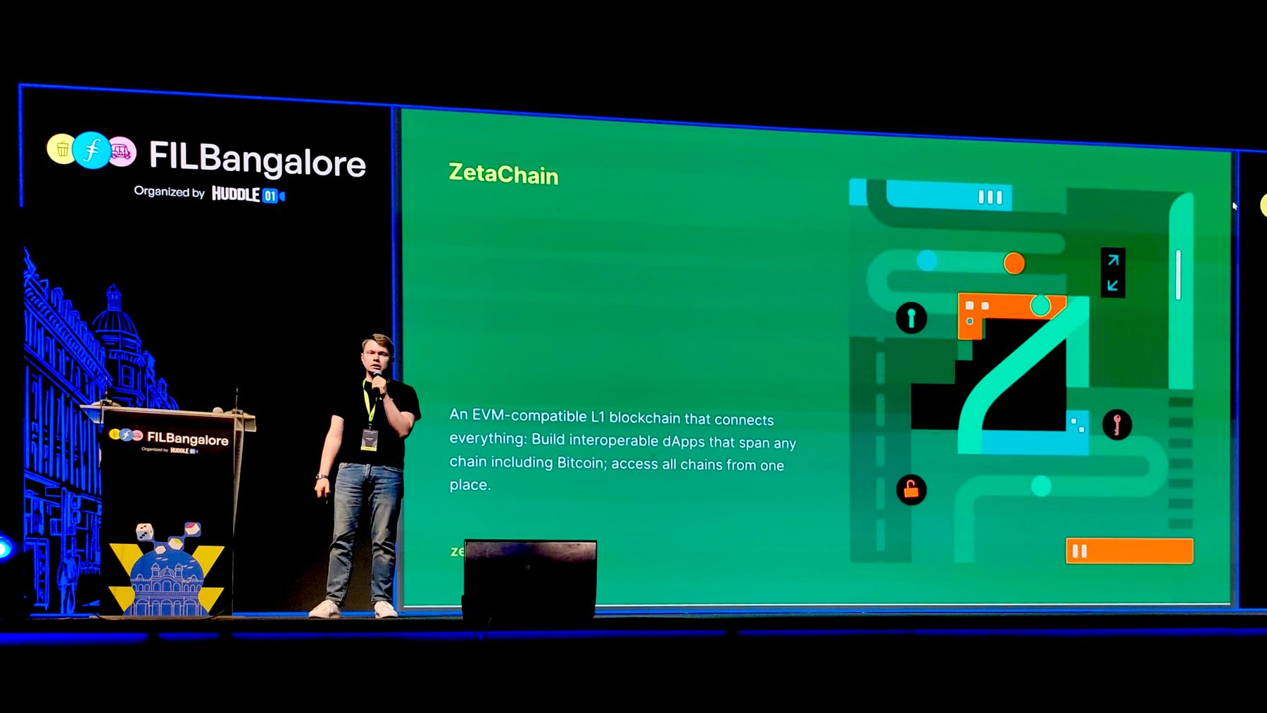 Denis speaking on a dark stage beside a large slide introducing ZetaChain