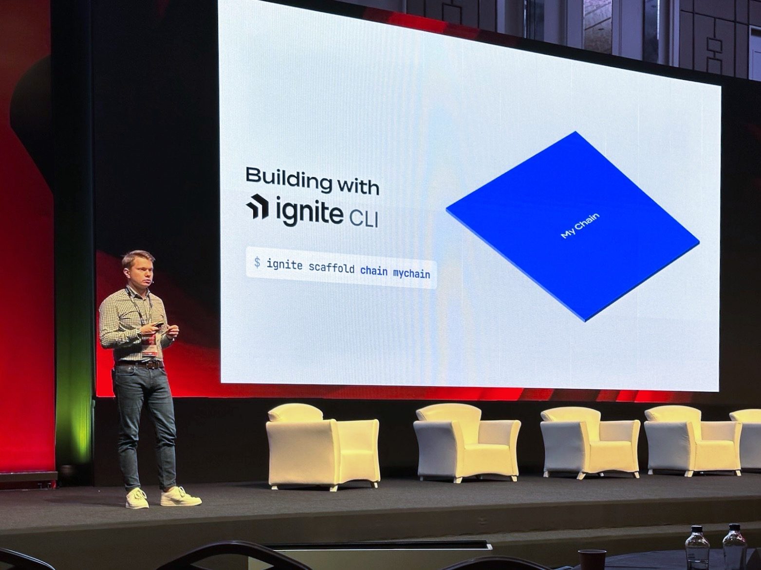 Denis on stage beside a slide reading “Building with Ignite CLI” and the command ignite scaffold chain mychain